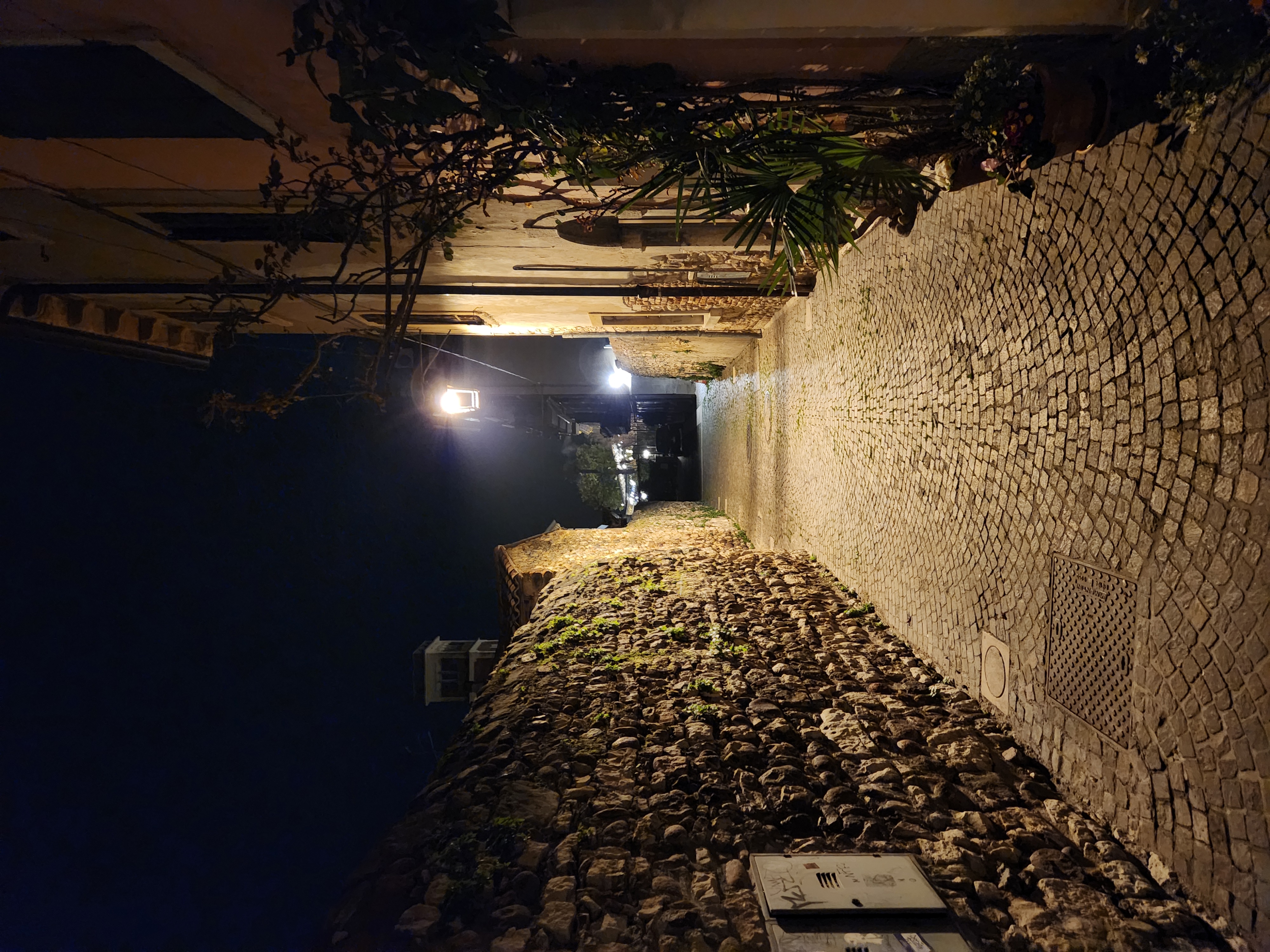 Ruelle pavée nocturne de Lazise, murs en pierre et lanterne, lac de Garde