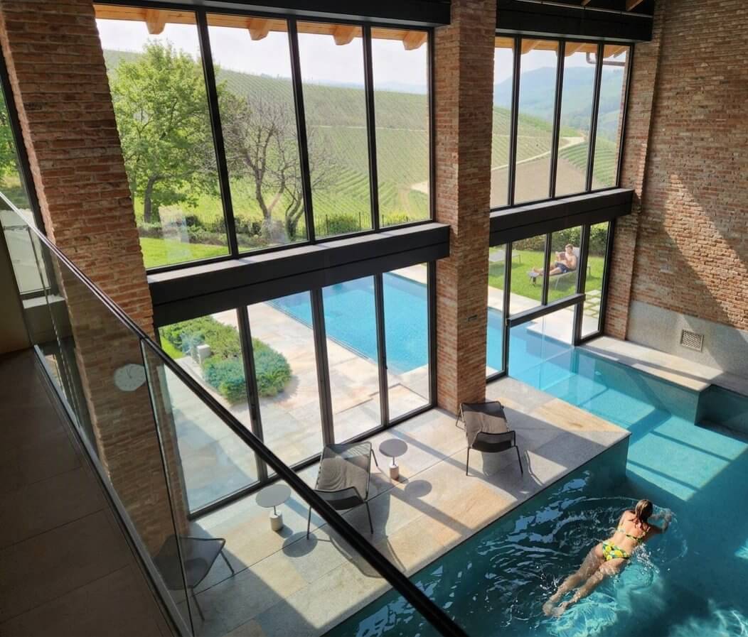 Piscine intérieure du spa avec murs en brique et vue sur les vignobles, resort du Piémont