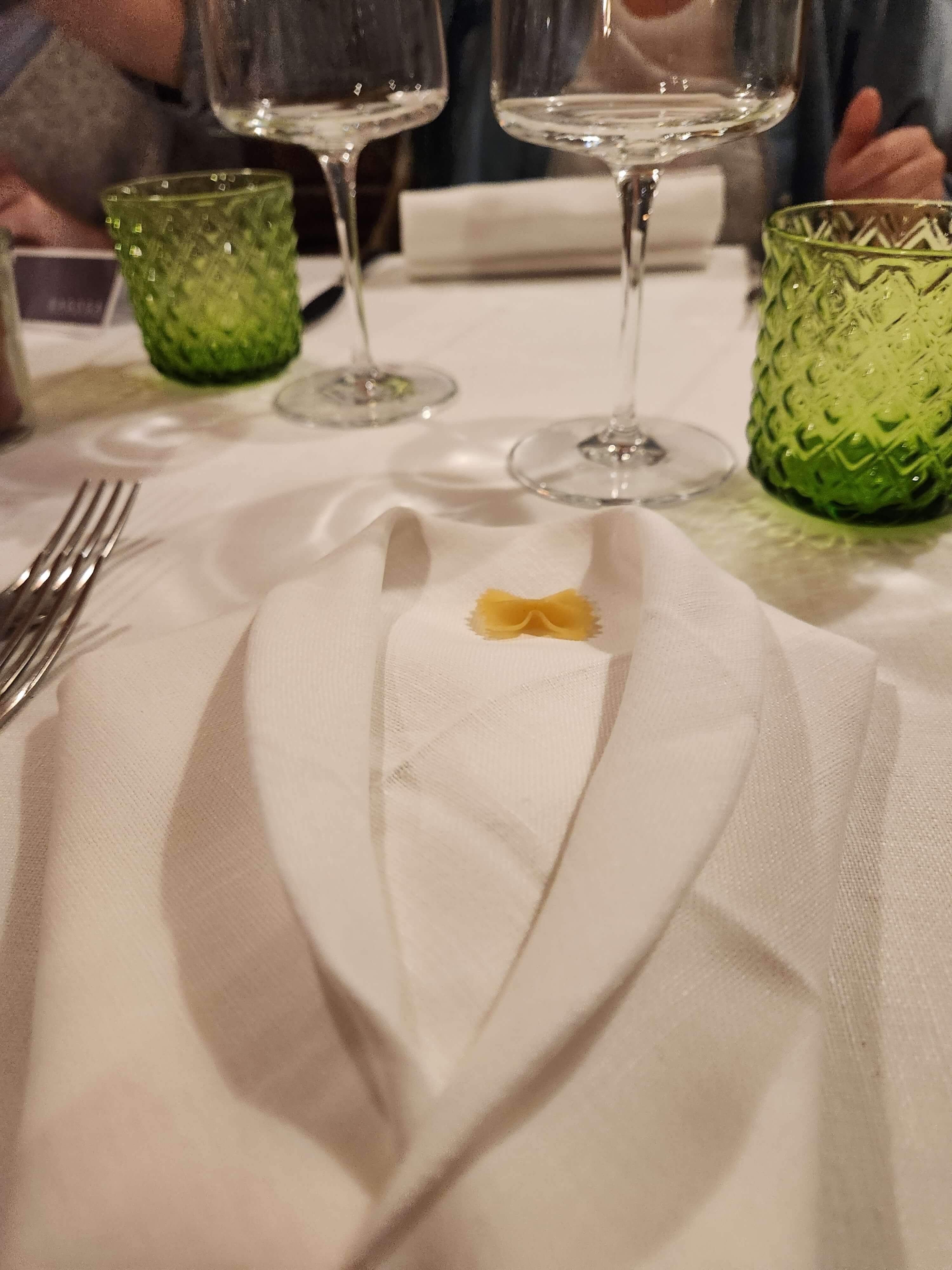Table dressée dans l'osteria toscane, serviette blanche avec une farfalle crue posée dessus